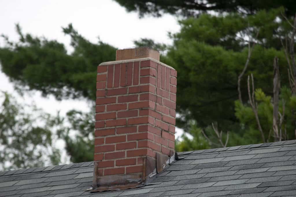Damaged and old roofing shingles and brick chimney on a house