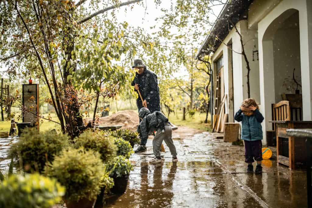 Son helping father and sweeping water from flooded yard on rainy day; yard drainage problems concept